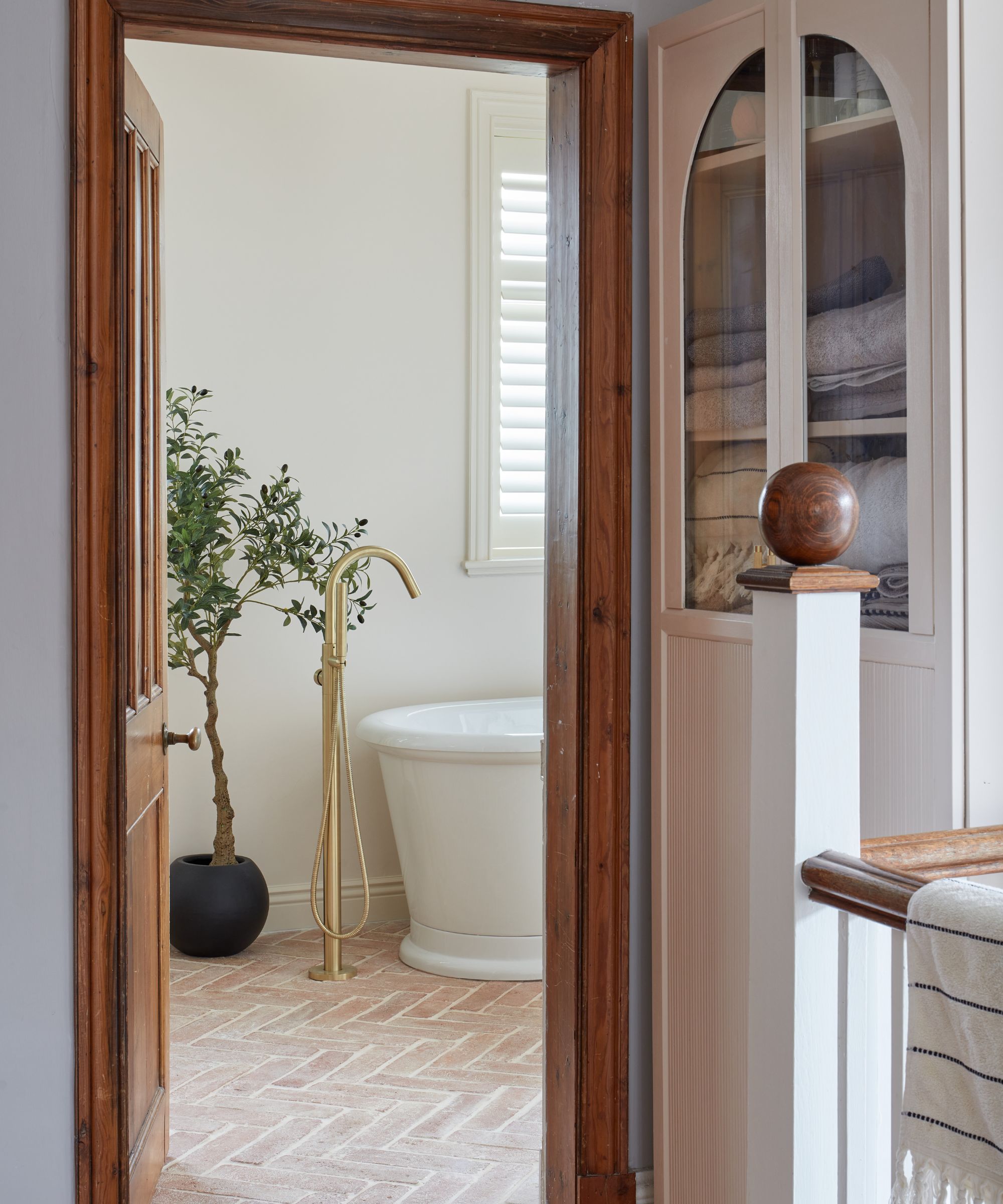 rustic bathroom with terracotta herringbone floor tiles, a freestanding bath tub with brass tap and a small olive tree