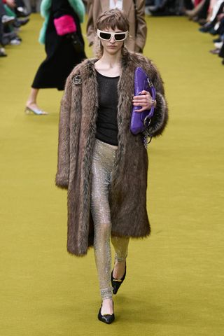 model wears crystal leggings, a black top, and coat at Gucci's fall winter 2023 show