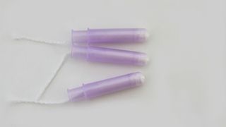 Three purple tampons with plastic applicators on grey background