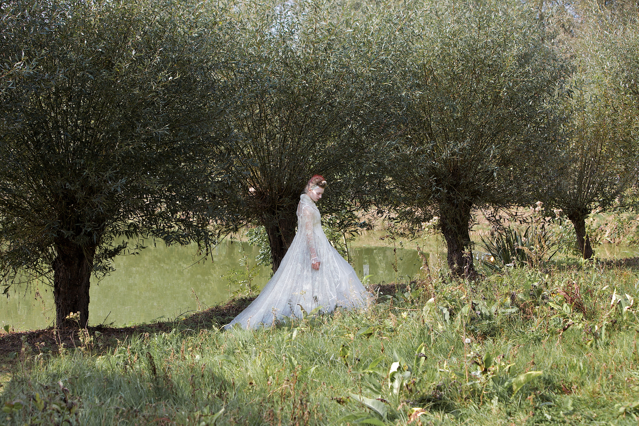 A woman in a wedding dress stands against a hedge