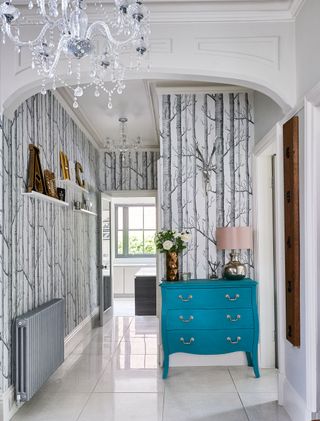 an elegant hallway with tree wallpaper, bright blue storage and chandeliers