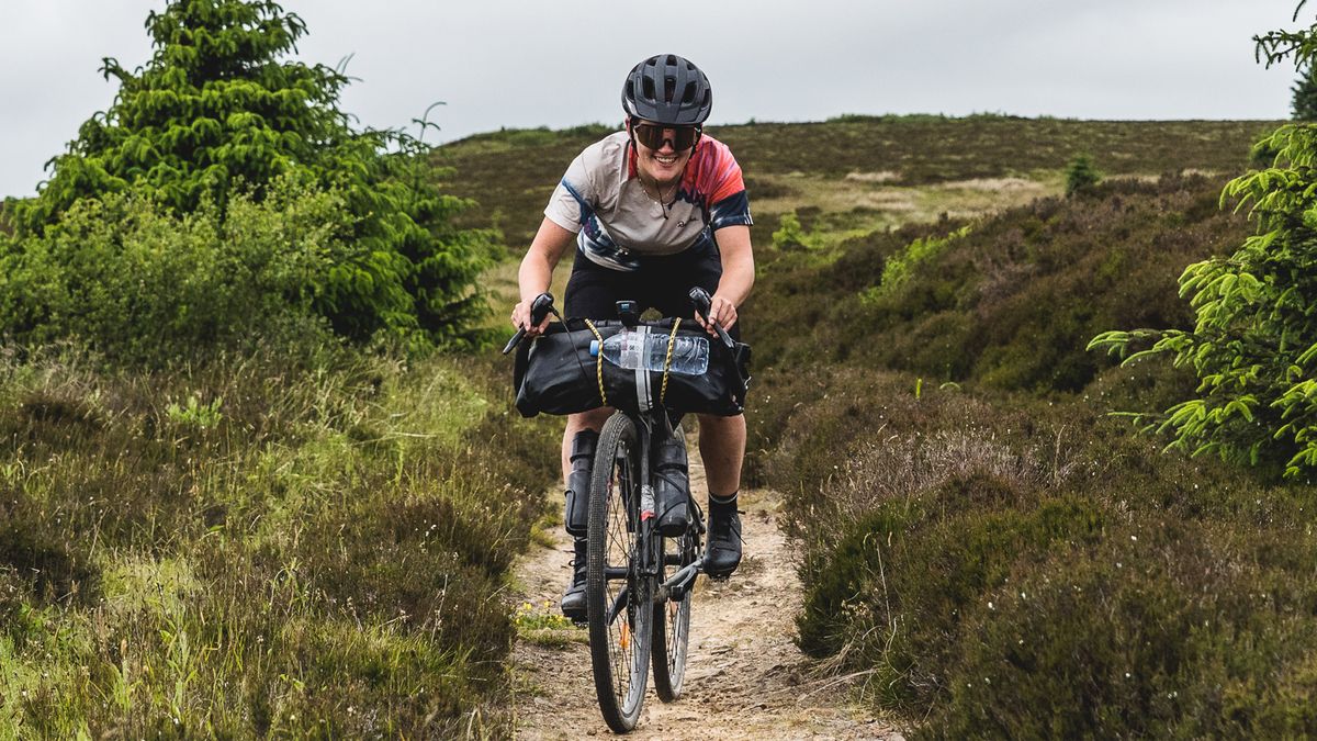 A female cyclists rides down a narrow dirt track