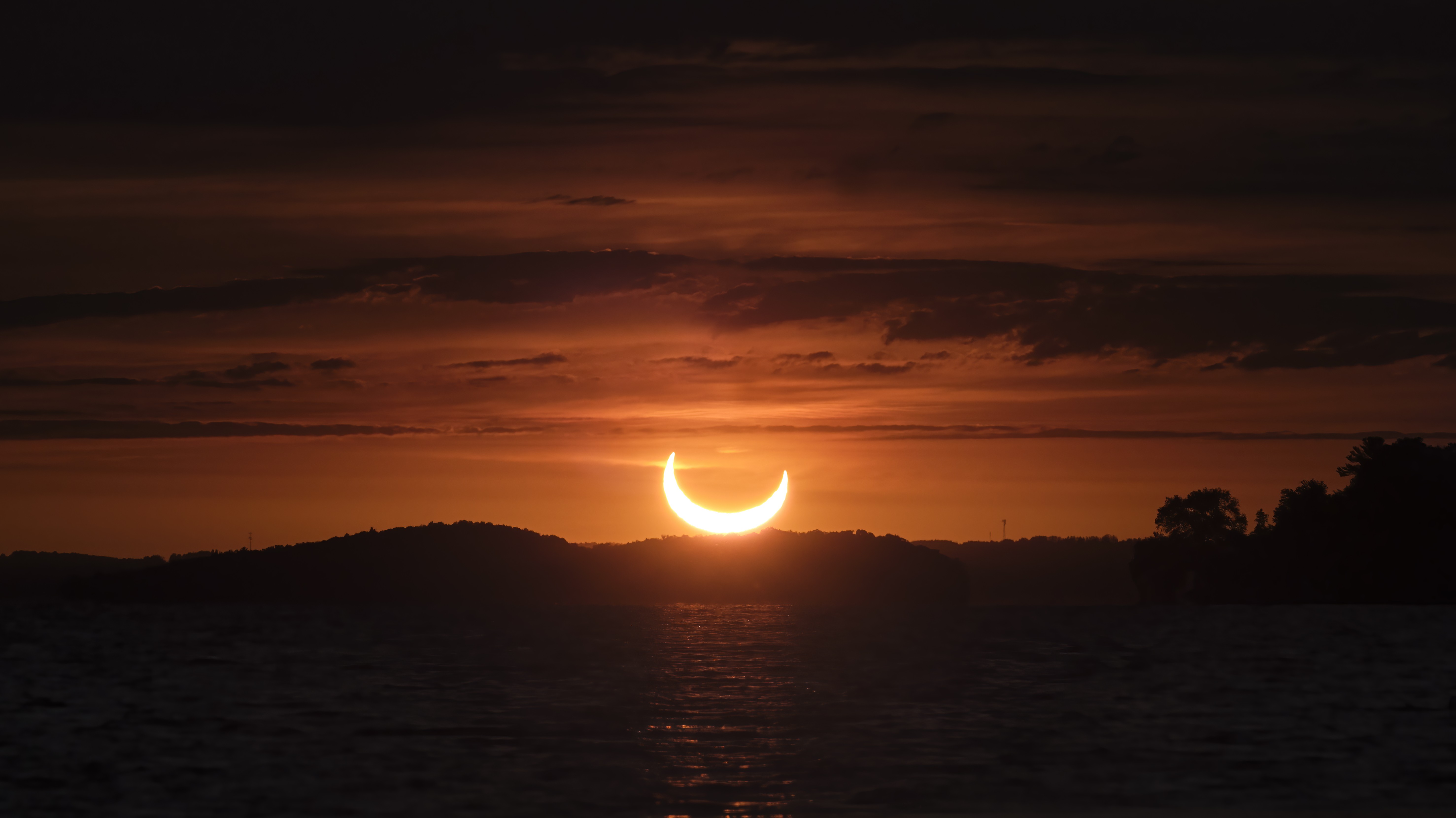 a partial solar eclipse at sunrise, the sun looks like a large bright crescent in the early morning sky as it rises above the horizon.