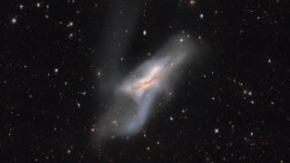 a wispy white galaxy is seen against the background of space. In space, a bunch of other bright dots and lines represent galaxies and objects across the universe, accidentally captured in this image.