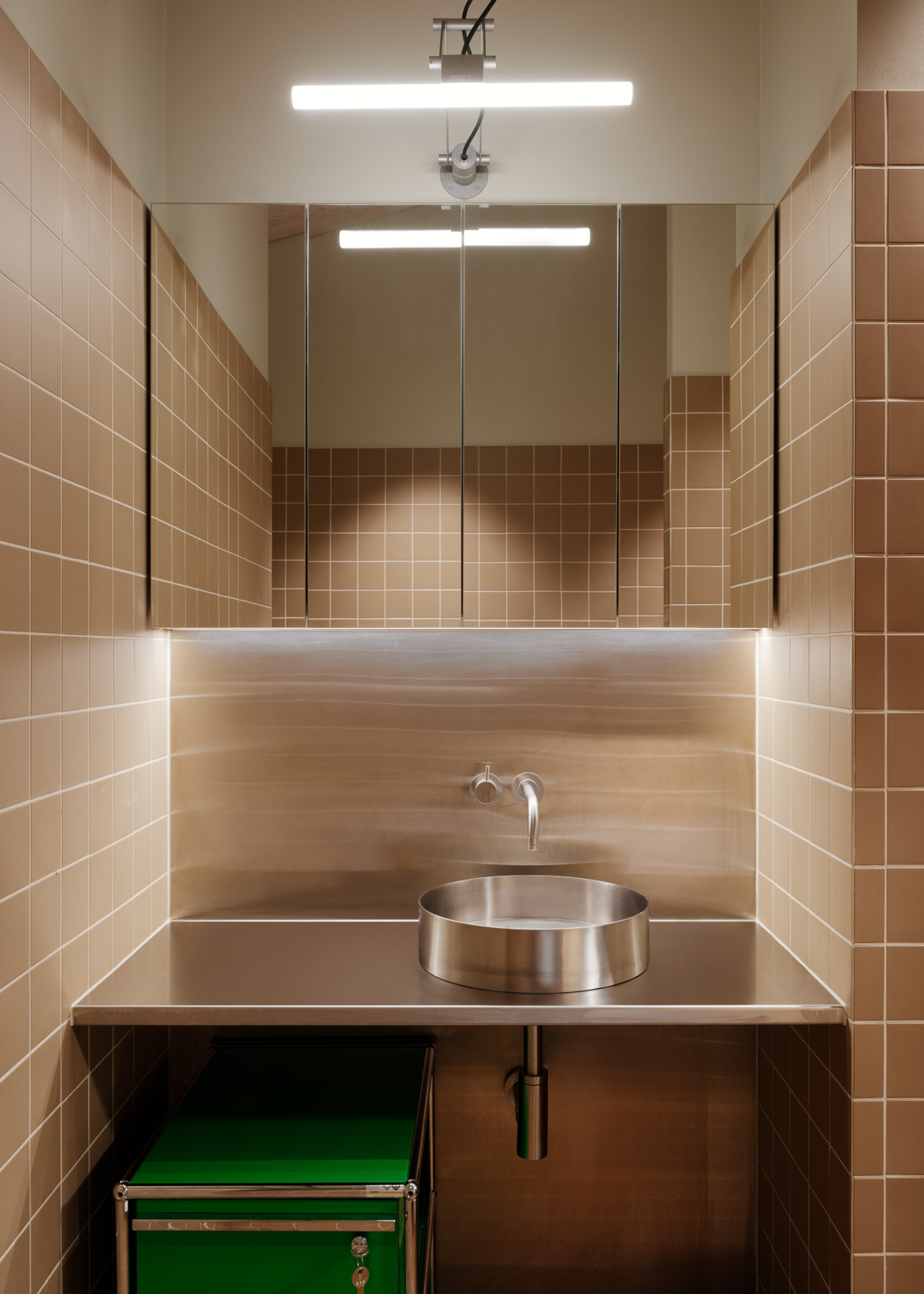 A bathroom vanity with beige square tiles and a steel sink and vanity