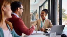 An adviser smiles as she shakes hands with a new client in her office.