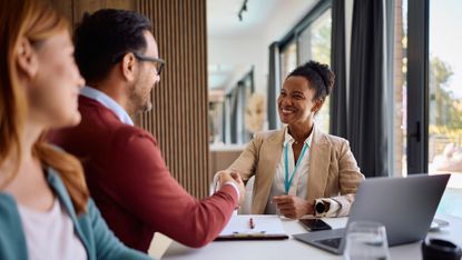 An adviser smiles as she shakes hands with a new client in her office.