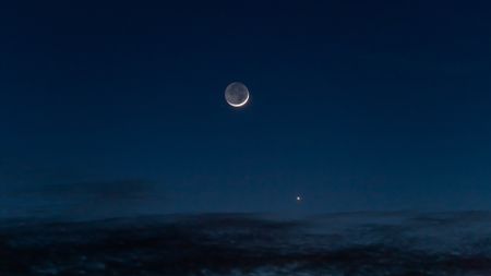 Moon in night sky above ocean.