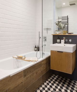 White built-in bath with glass shower screen and shower tap next to white wash basin on top of wooden bathroom cupboard