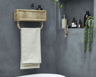 A gray concrete effect bathroom with cane shower shelf with towel rail feature