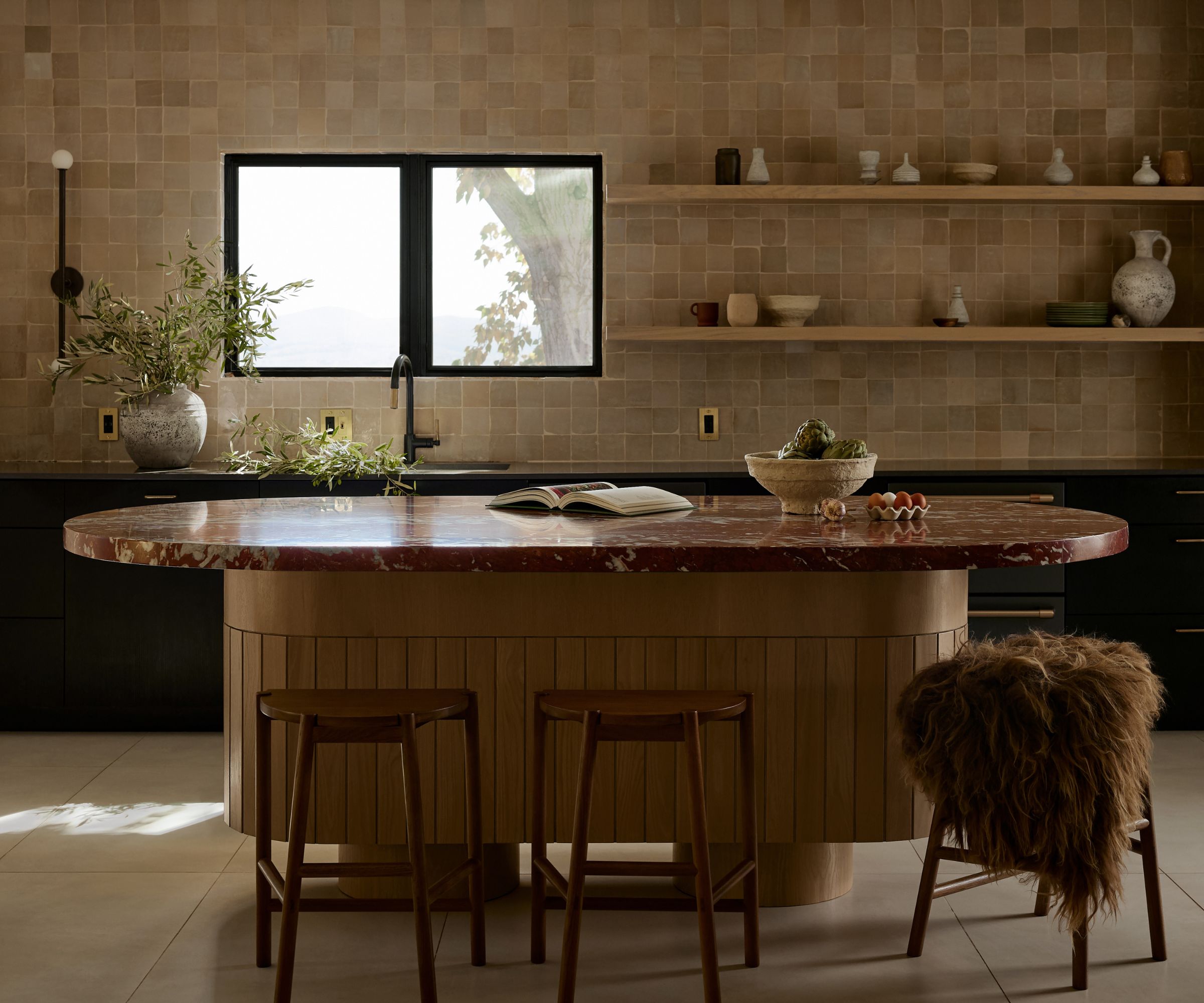 A neutral kitchen with black cabinets and a curved wooden island topped with a burgundy marble countertop