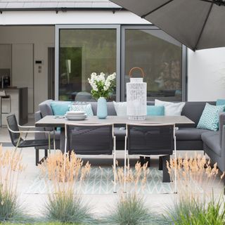 Outdoor paved area with grey outdoor sofa and umbrella overhead