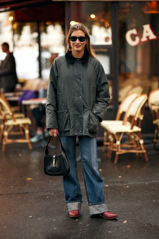 A woman wearing a fall outfit idea of blue jeans, a green collard barn jacket, and red cowboy boots at Paris Fashion Week.