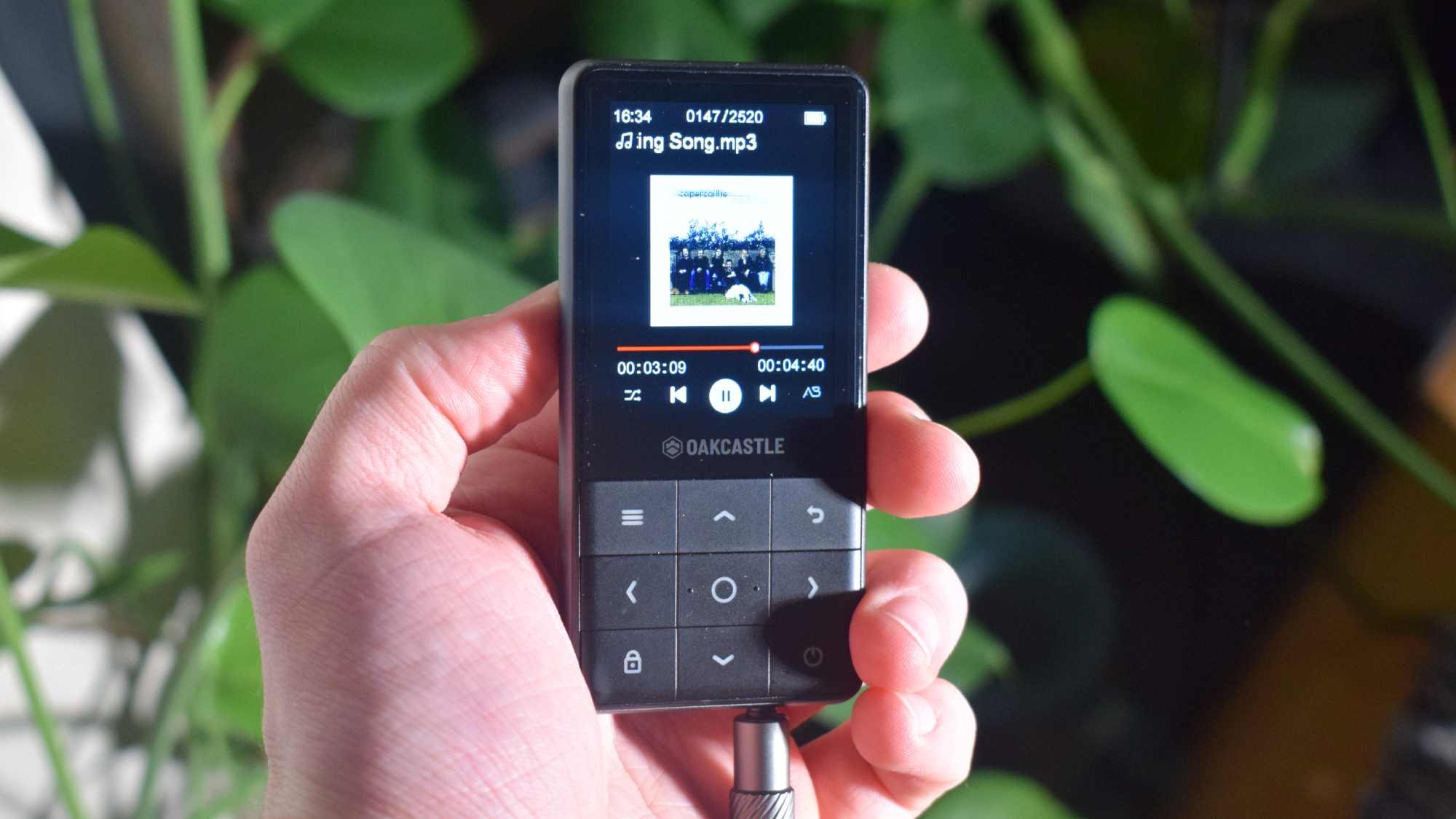 The Oakcastle MP300 in a hand, with an aux connected, playing folk music.