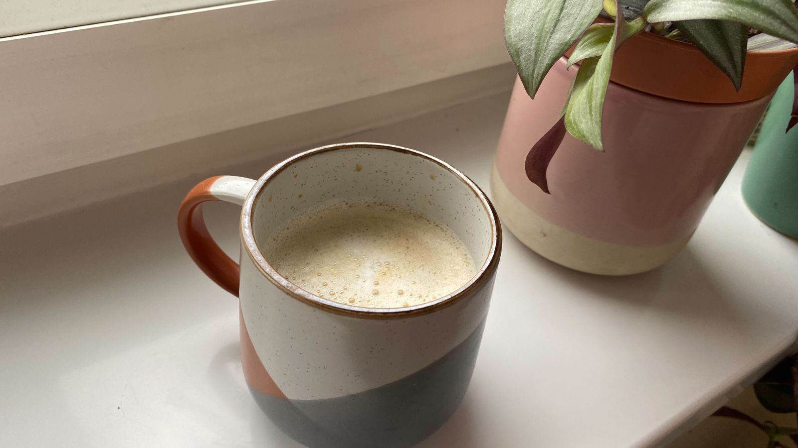 A cup of coffee on a windowsill next to a plant pot.