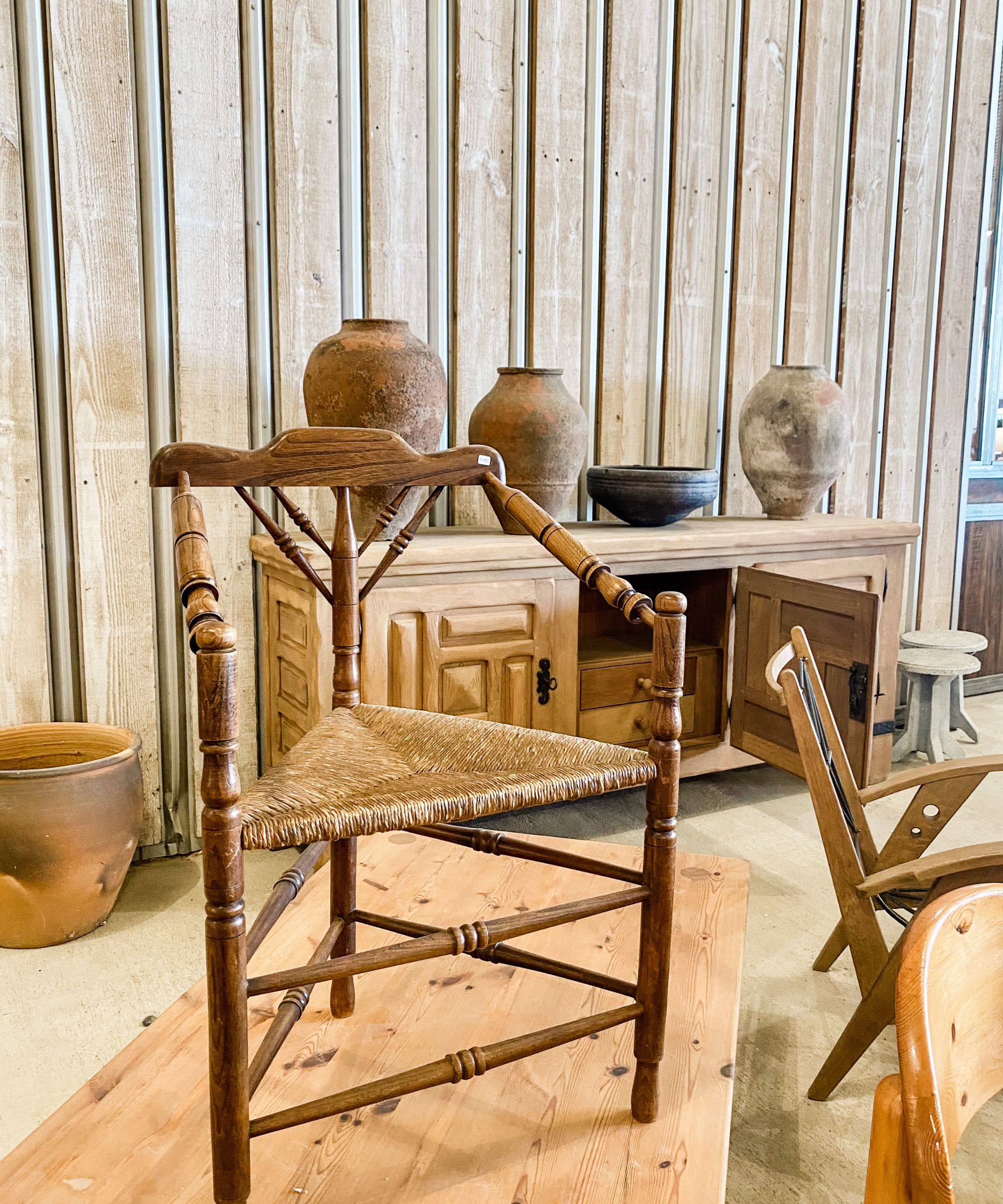 Vintage wicker chair in a room with wood panelled walls and a vintage wooden console in the background with some vintage pottery on top