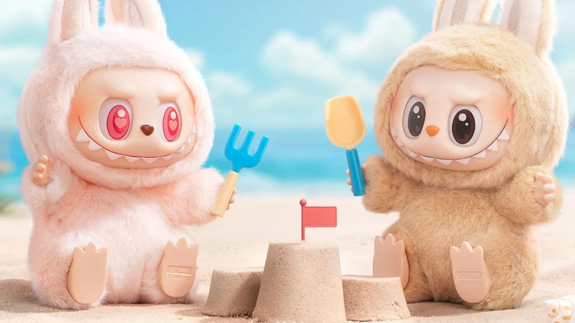 Two Labubu dolls sat at a peach with sandcastles and tools