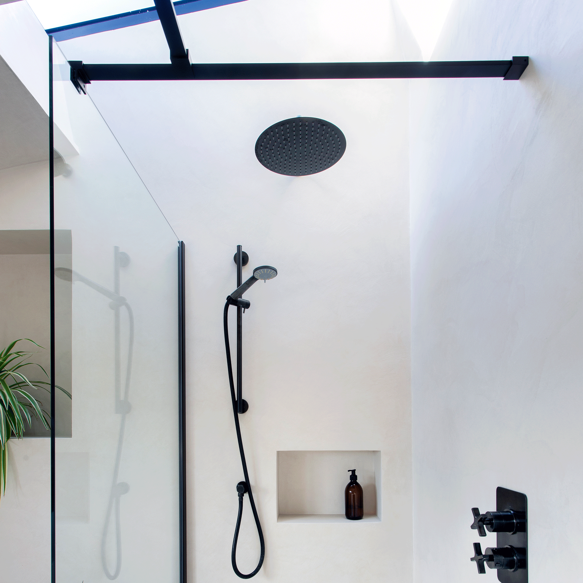 a bathroom with a glass shower panel and black shower fixtures with a roof light above it