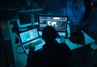 Image of a cyber criminal using several computers in a dark room 