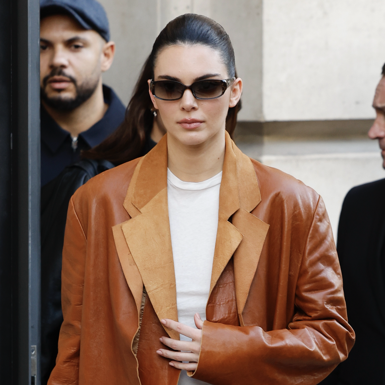 Kendall Jenner wears white top, brown leather double blazer, brown suede Hermès bag, black trousers, black boots, black sunglasses, outside Schiaparelli, during Haute Couture Spring-Summer 2025 as part of Paris Fashion Week on January 27, 2025 in Paris, France