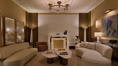 A golden-lit living room with oversized couches, paintings hanging on the walls, a marble fireplace, and a bass-relief wall.