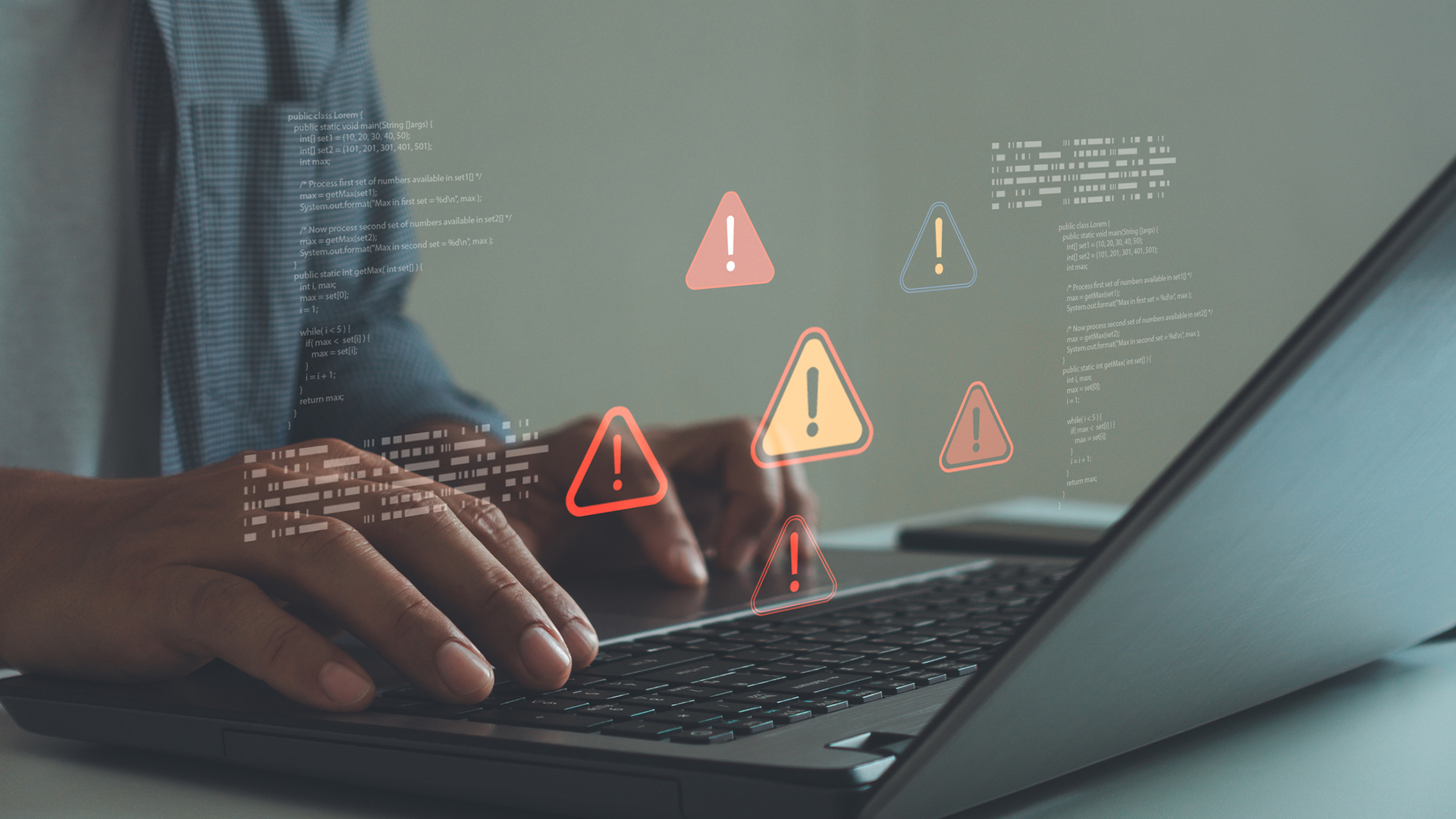 A person types on a laptop keyboard. Above the keyboard, various warning signs hover in a depiction of cybersecurity threats