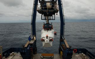 The submersible Alvin is lowered into the water, where swimmers will disconnect the lines and communicate with the pilot inside to ensure that the sub is ready for descent.