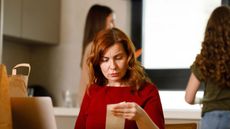 Woman checks grocery bill in kitchen with daughters in background