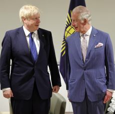 Boris Johnson wearing a navy suit and tie standing next to King Charles and looking at him quizzically 