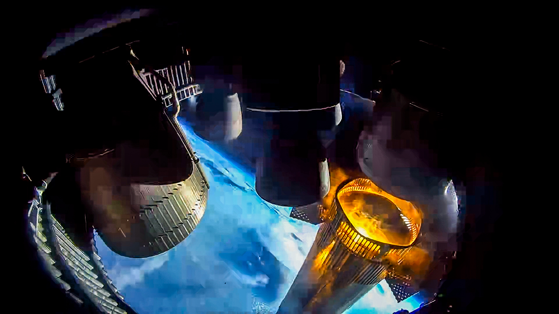 view from a spacecraft's engine bay showing a large metallic silver rocket booster, with orange flame licking its top, falling away with earth in the background
