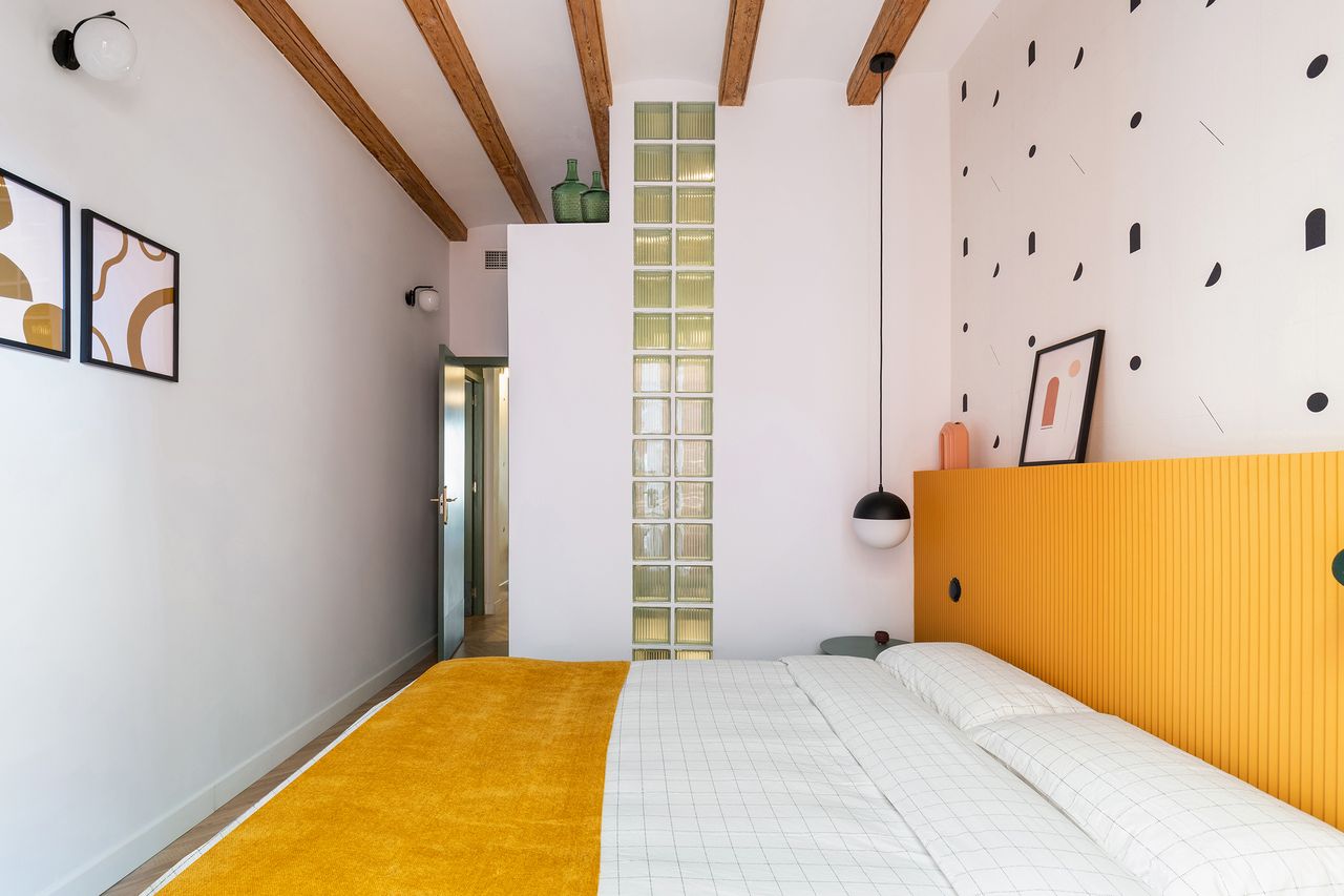 A bedroom with yellow headboard, wooden flooring and wooden ceiling beams