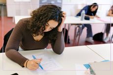 A teenage girl looking stressed while doing a test in a classroom