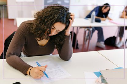 A teenage girl looking stressed while doing a test in a classroom