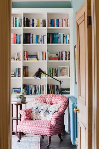 open door to room with high bookshelves and armchair with pink cover