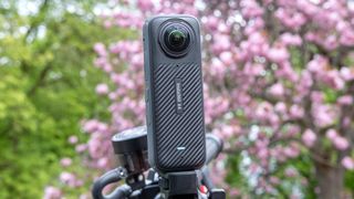 A photo of the Insta360 X4 mounted to motorcycle handlebars with green foliage and a pink blossoming tree in the background