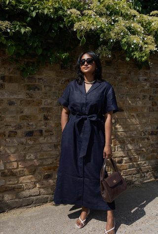 a woman's shirtdress outfit with a navy linen dress styled with a gold collar necklace and white strappy sandals and a brown bag