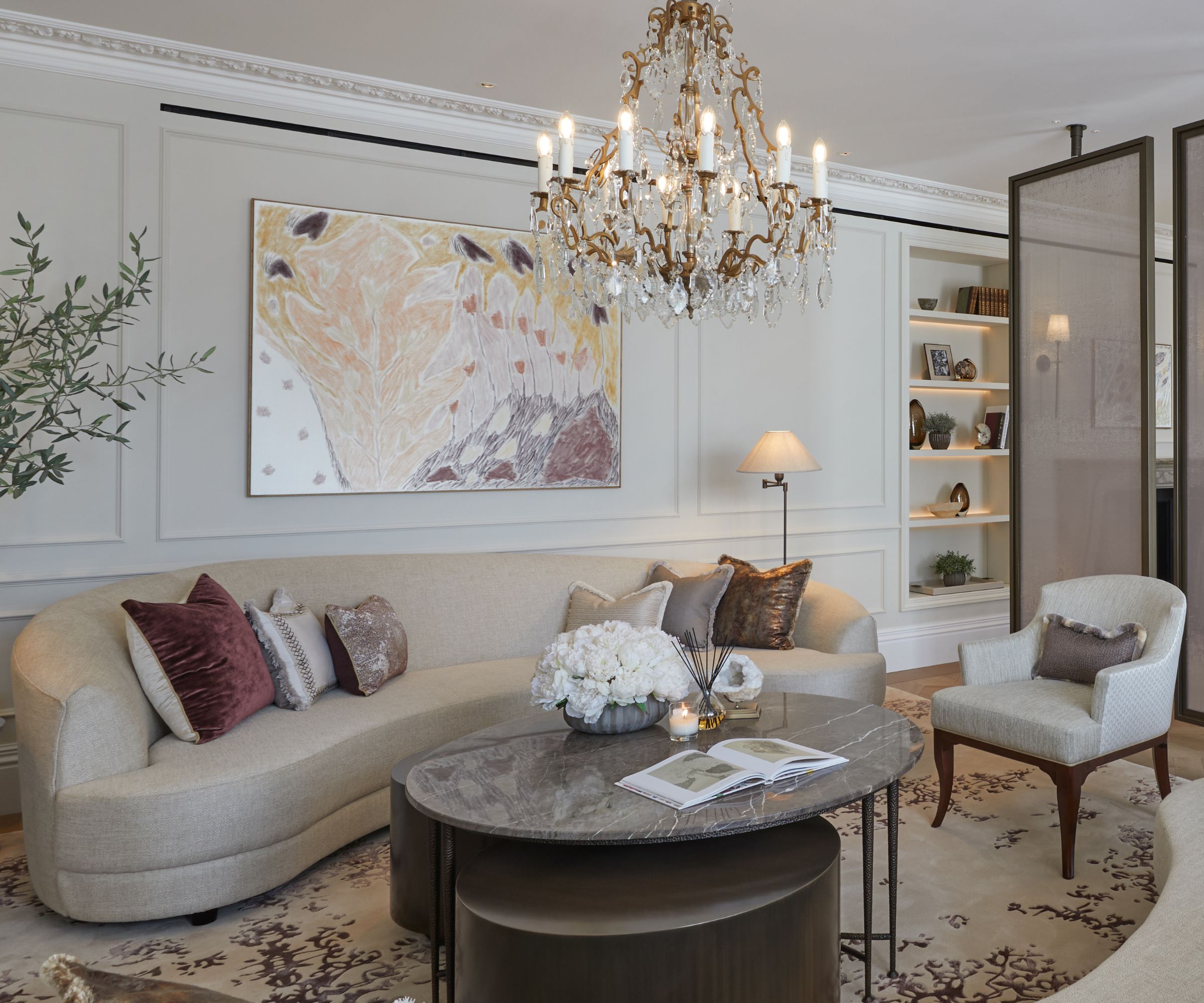 Modern living room with sculptural curved beig sofa, large artwork hung above on panelled walls, round coffee table and rug, armchair to the right hand side
