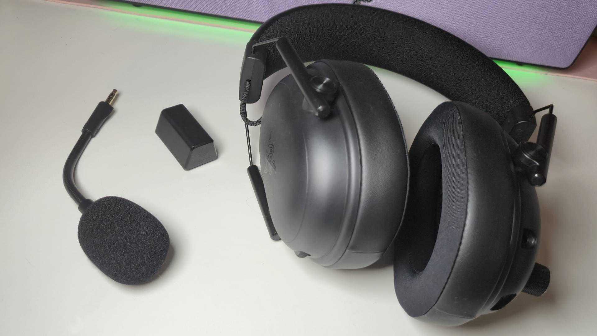 Photo by Rosalie Newcombe of the Razer BlackShark V3 gaming headset sitting on a white desk with a green glow above it.
