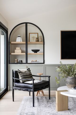 living room with sage green cabinetry, alcove with shelves and crittal doors, black retro armchair