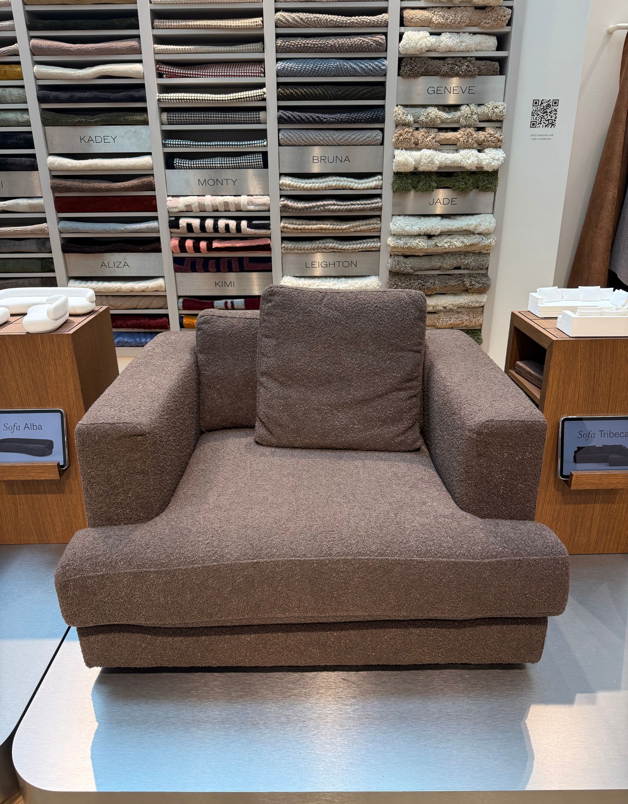 A brown lounge chair with a brown cushion sitting in front of a shelving unit filled with folded fabrics
