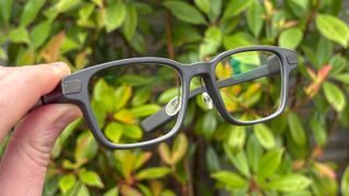 Even Realities G1 Smart Glasses held by fingers with green bush in background