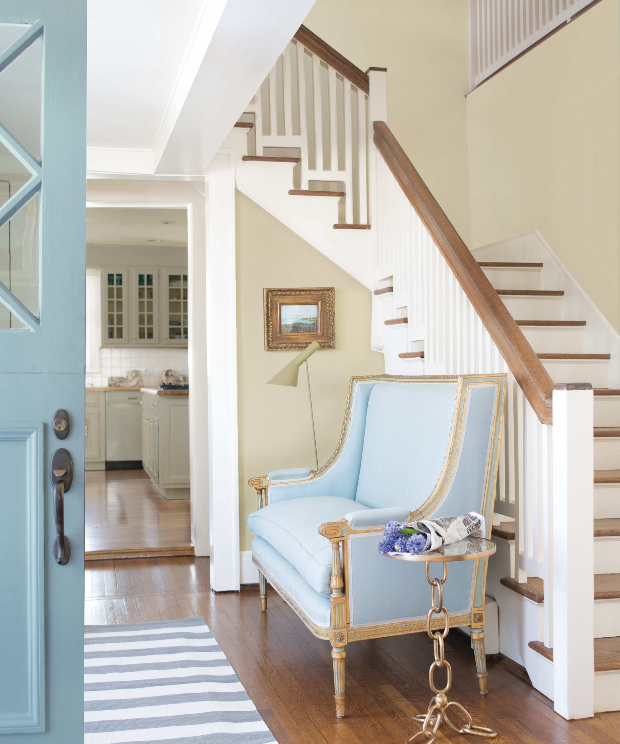 Entryway with Pashmina by Benjamin Moore painted walls, white staircase, wooden floorboards, a pale blue bench with a side table, and a pale blue front door.