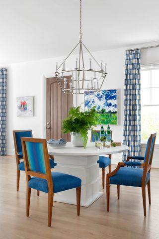 A white dining room with bold blue accent on dining chairs, curtains and artwork