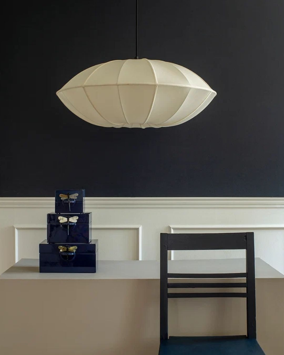 Lamp Shade Indochina Off White UFO, installed against a black and white background wall, atop a gray podium topped by blue boxes and behind a black, geometrical chair.