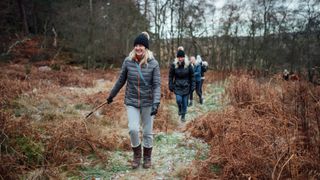 Woman walking with stick through forest, learning to work out in winter with friends