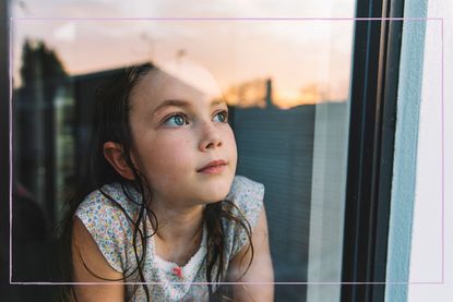 A young girl looking through a window at a sunset