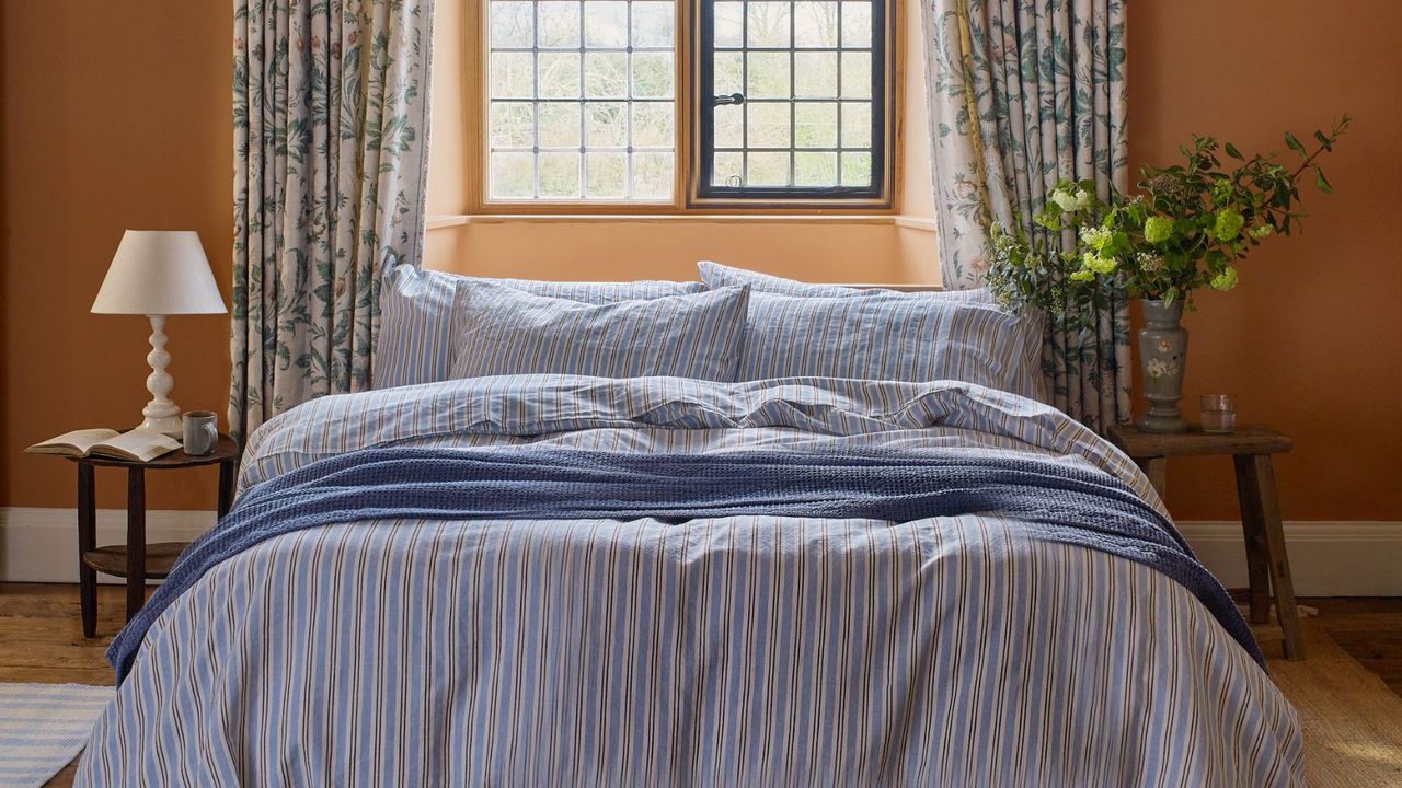 A bed with blue striped linens, a bedside lamp and a vase of flowers