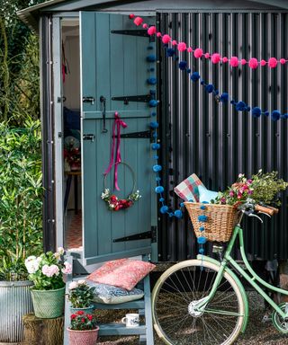 A corrugated black shed with colorful garlands and a mint green vintage bicycle