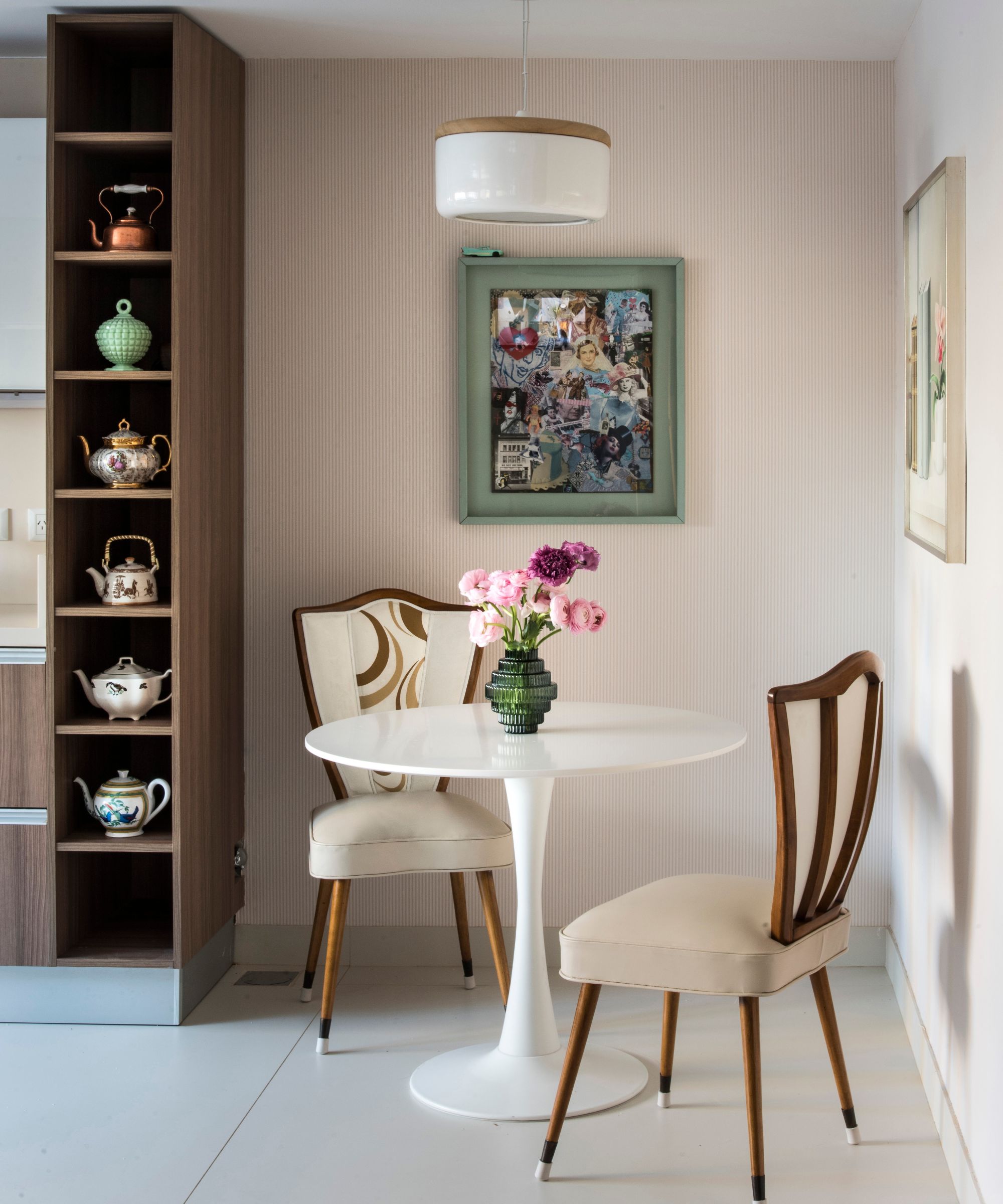 A small kitchen eat-in area with a white round table, wood-framed chairs, and pink striped wallpaper