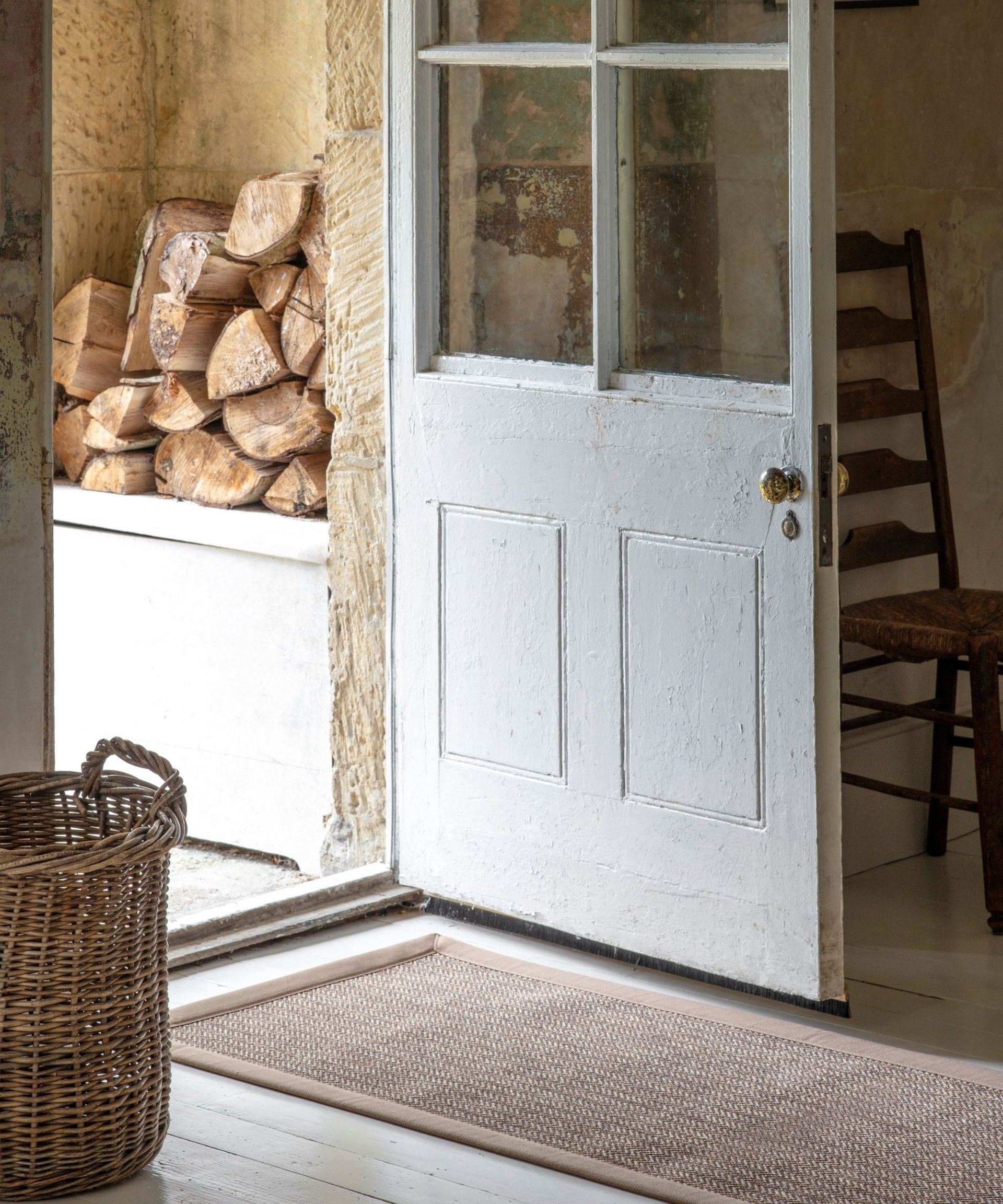 A mudroom with an open white door, a woven rug on the white floor, and a basket and brown chair